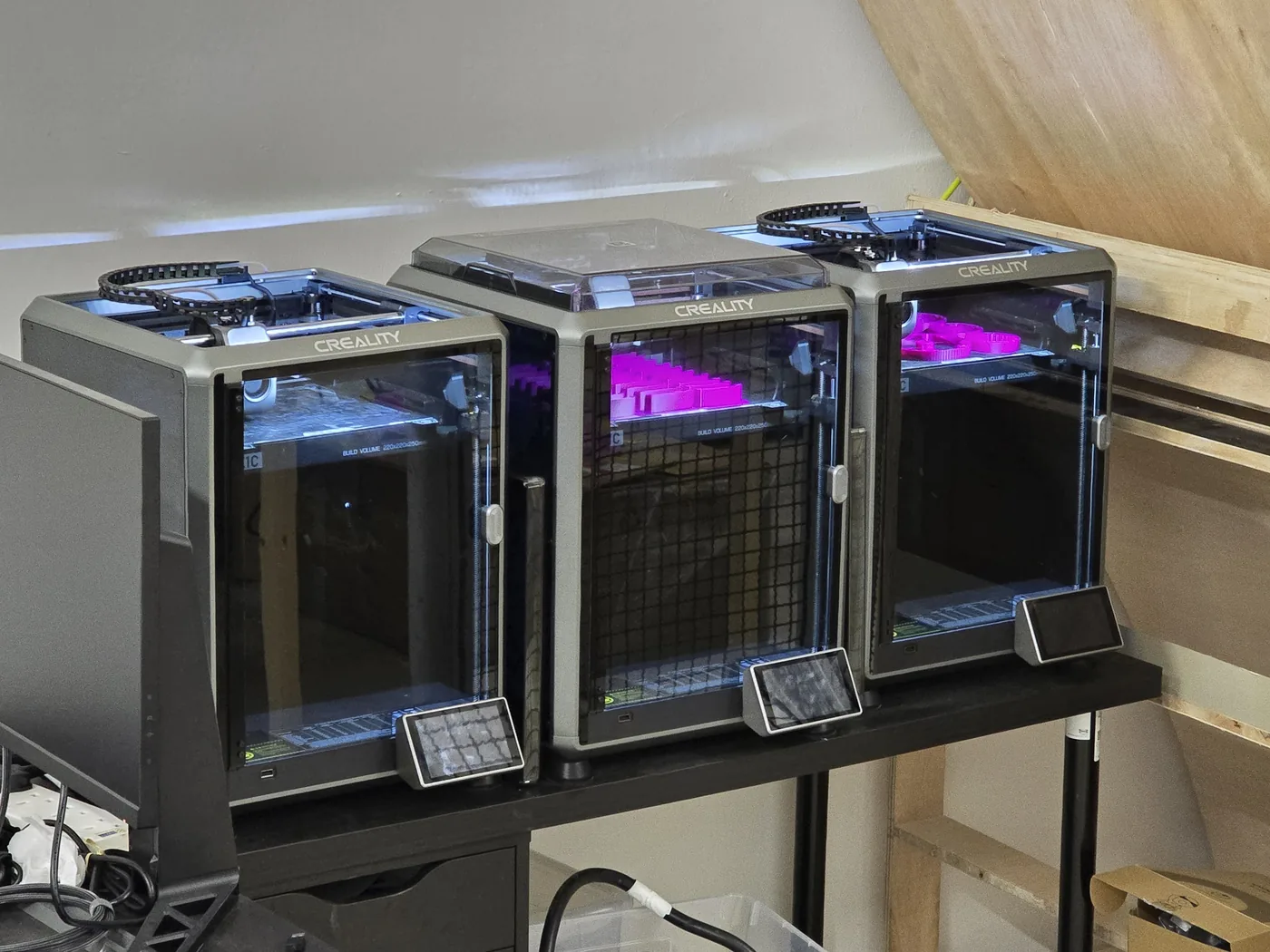 Drei 3D-Drucker im Dauerbetrieb, magentafarbenes Filament in den Bauräumen.