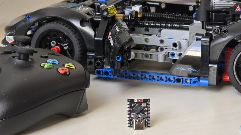 Xbox-Controller, eine daumennagelgroße ESP32-C3-Platine und ein LEGO-Technic-Auto nebeneinander auf einem Schreibtisch.