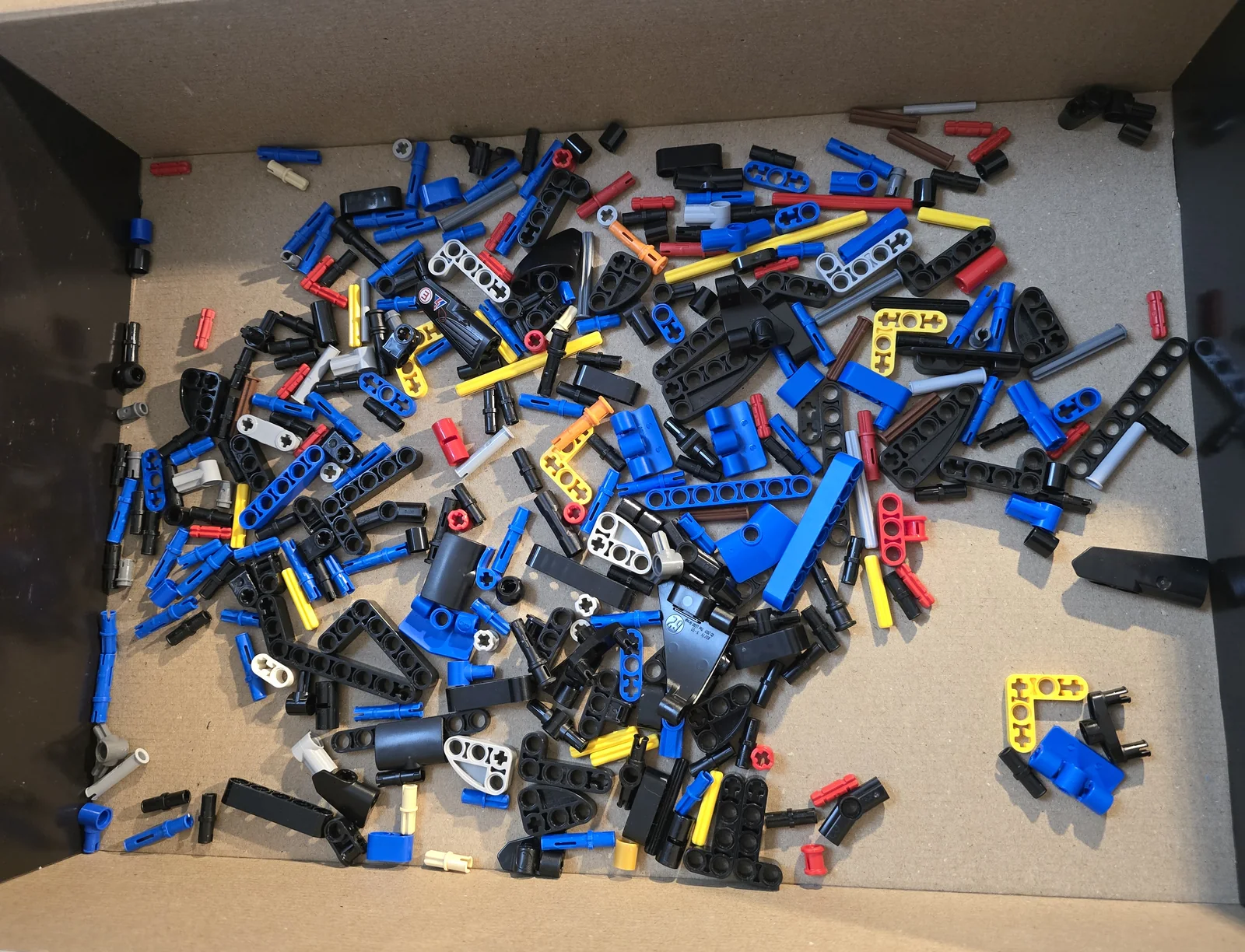 Blick von oben in einen Karton mit mehreren hundert LEGO-Technic-Teilen in Blau, Schwarz, Rot und Gelb.