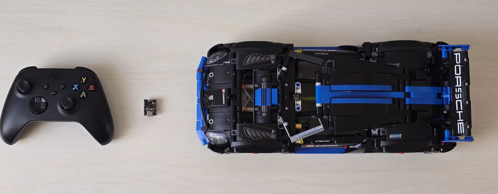 Draufsicht auf einen Schreibtisch: links ein schwarzer Xbox-Controller, in der Mitte eine daumennagelgroße ESP32-C3-Platine, rechts das LEGO-Technic-Auto von oben.